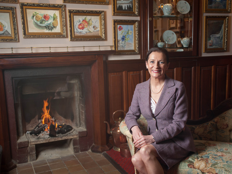 Women in lilac suit sitting by fire.