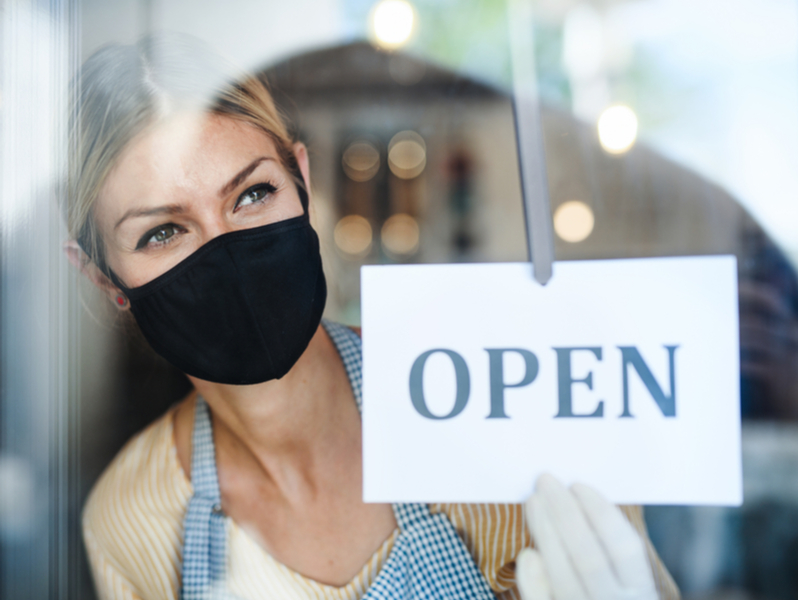 Woman in mask putting an open sign in window.
