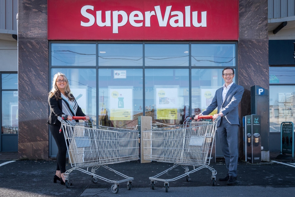 Woman and man standing outside SuperValu store with trolleys.