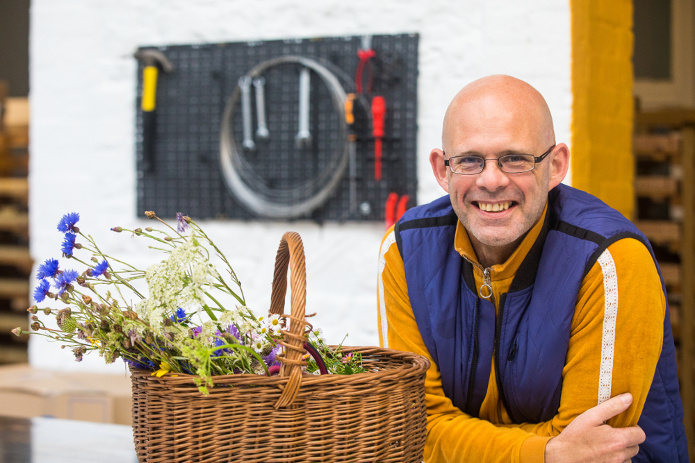 Smiling man beside a basket full of herbs and flowers.