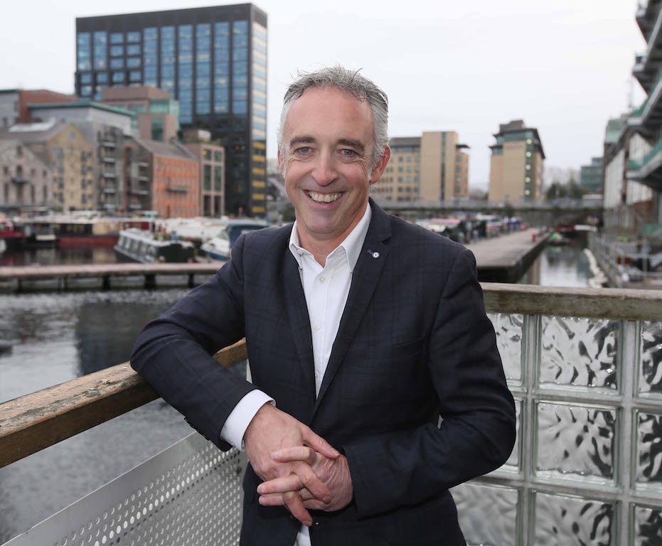 Smiling man in dark jacket leaning against a rail in Dublin.