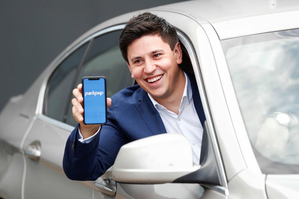 Man in blue jacket holding phone out of car.