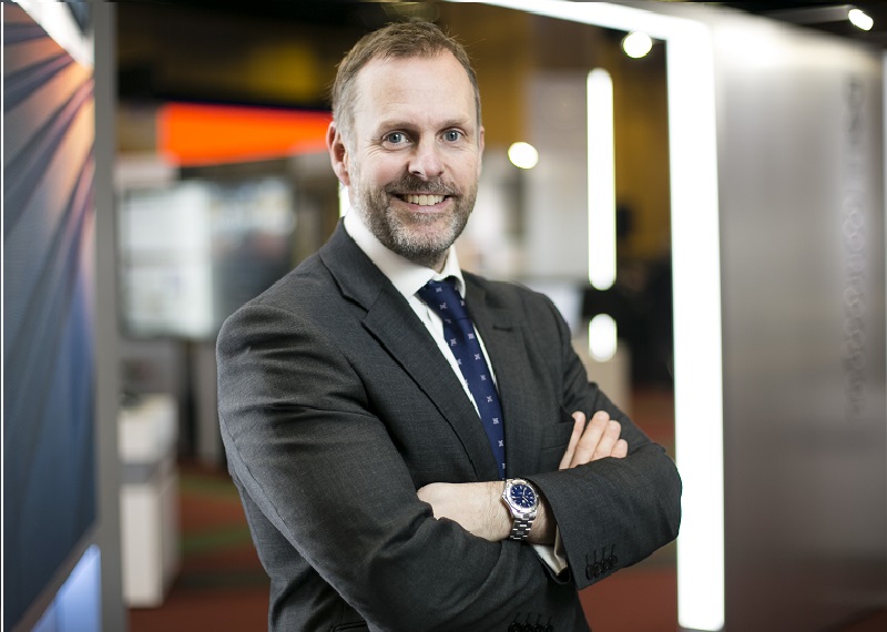 Man with beard in grey suit with arms folded.