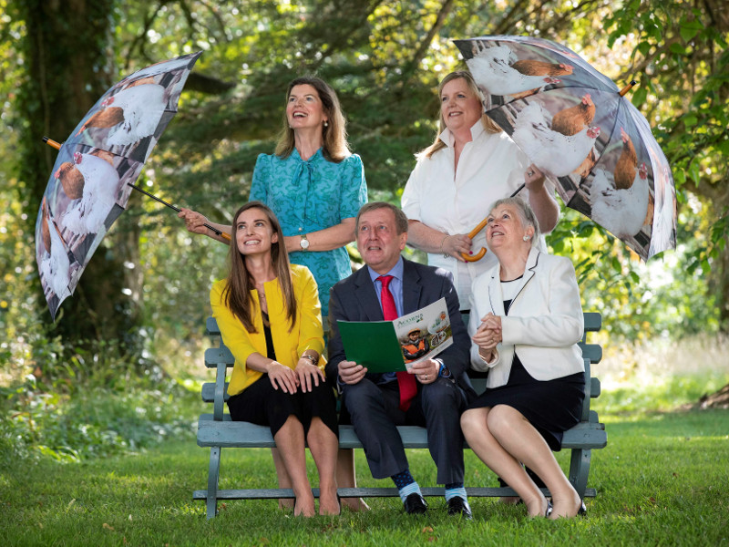 Four women and a man holding umbrellas in a wooded area.