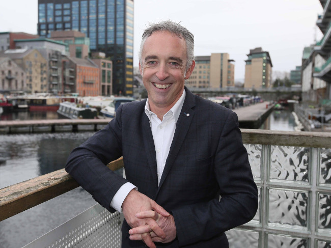 Man in navy jacket leans against rail in Dublin's docklands.