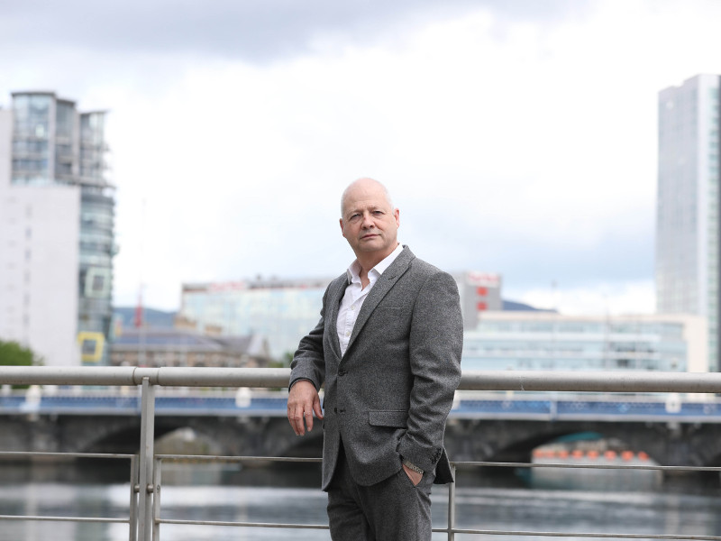 Man in grey suit leaning on a bridge in London.