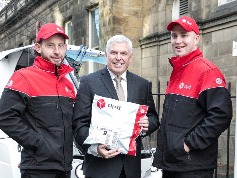 Two men in courier uniforms with one man in a suit holding a parcel.