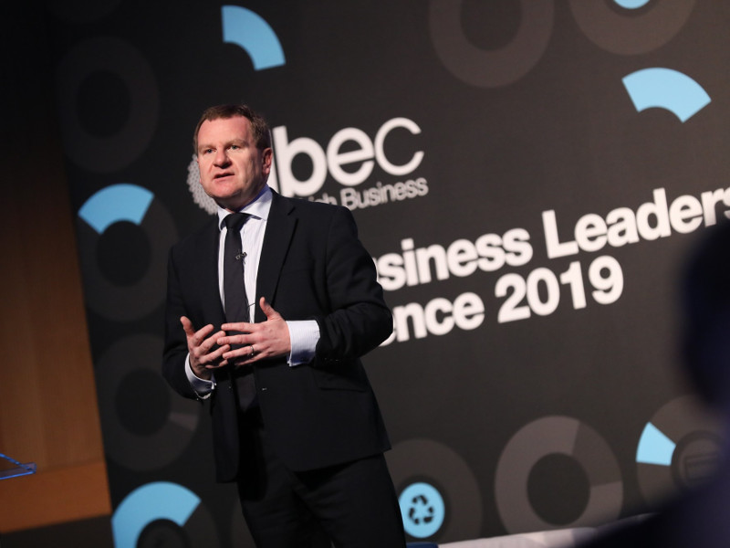 Man in dark suit standing on stage at a conference.