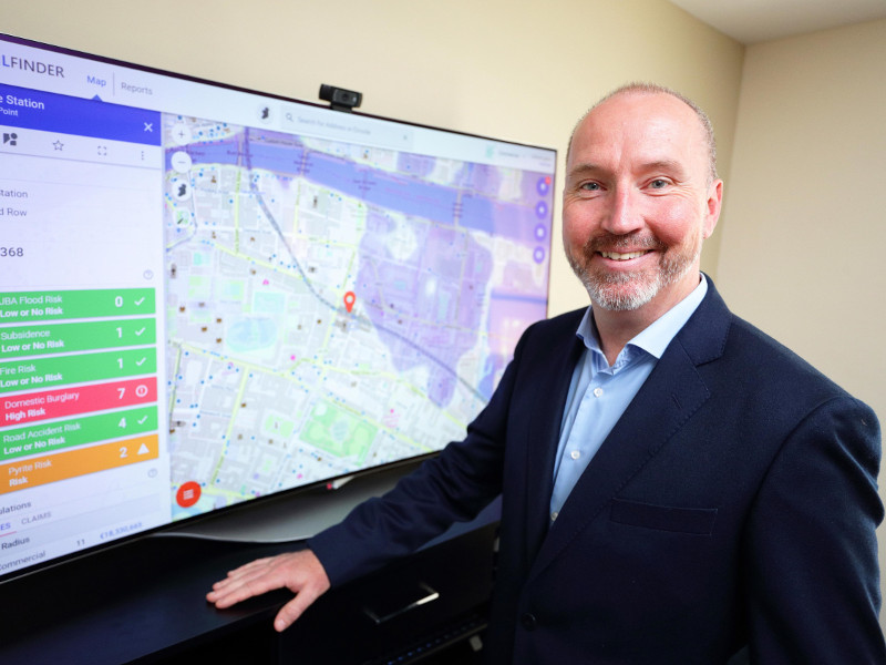 Man in navy jacket, grey beard, standing in front of a computer screen with location software.