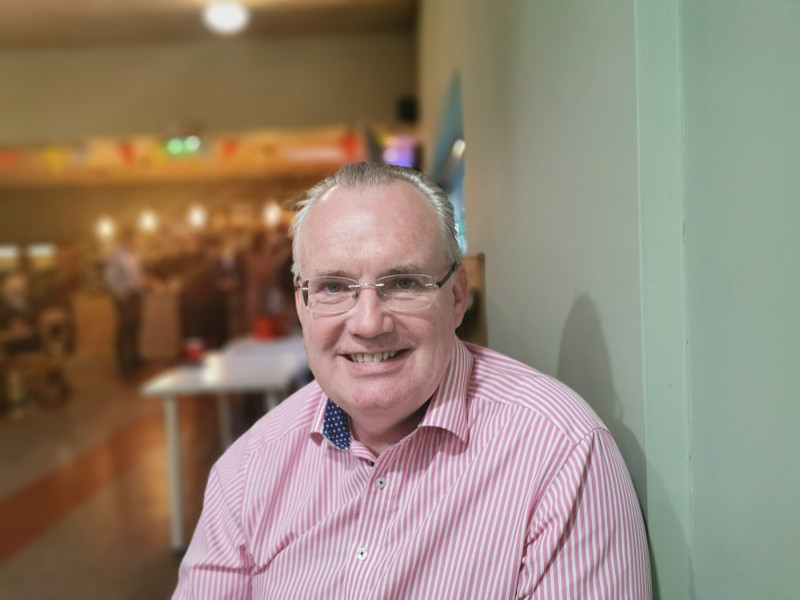 Man with grey hair, glasses and pink-striped shirt.