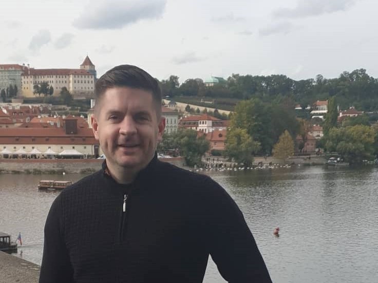 Man with black sweater standing in front of a marina.