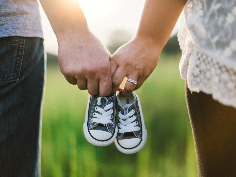 Married couple hold hands and baby booties.