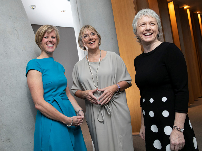 Three women in blue, grey and black dresses respectively.