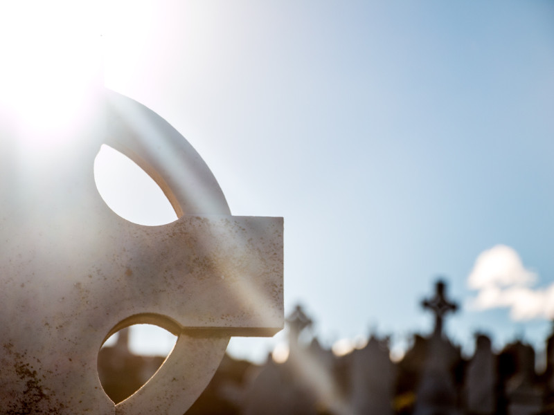 Sun shining through a celtic cross in a cemetary.