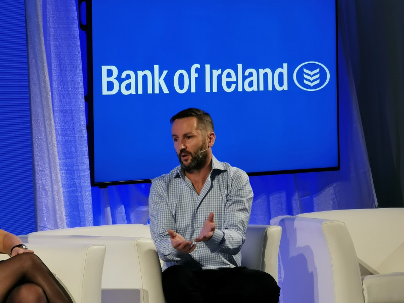 Man in blue shirt on white coach gesturing with hands while answering a question.