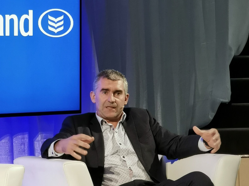 Man in white shirt and dark jacket talking.