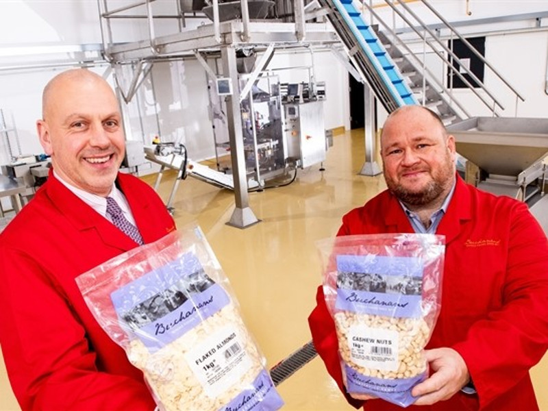 Two men in red factory coats holding bags of nuts.