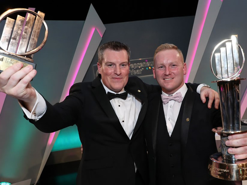 Two men in tuxedos holding awards.
