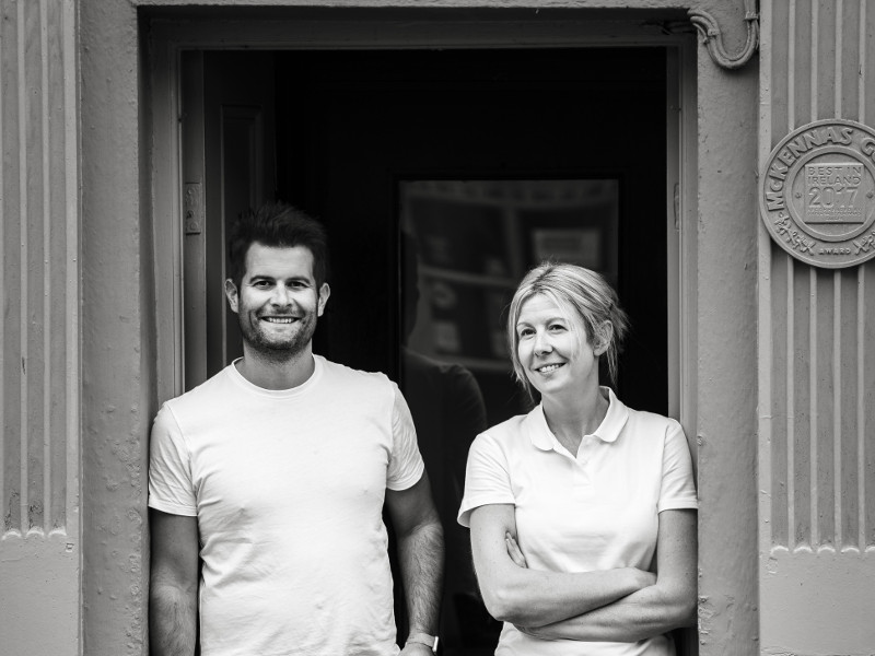 Black and white photo of a man and woman in white t-shirts standing in a doorway.