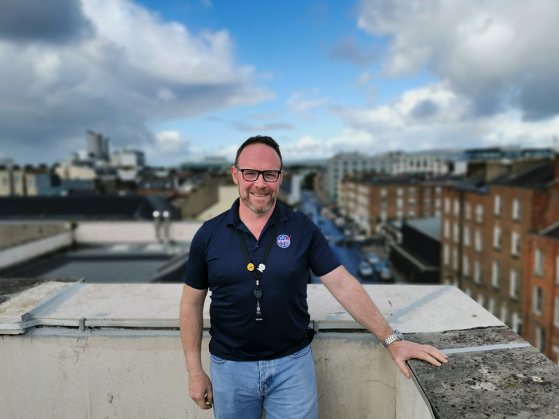 Man in navy t-shirt standing on a roof top in Limerick under a blue and cloudy sky.