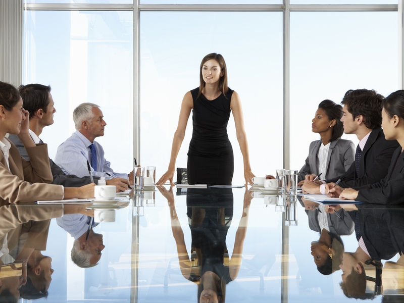 Woman in black dress stsanding up at a meeting.