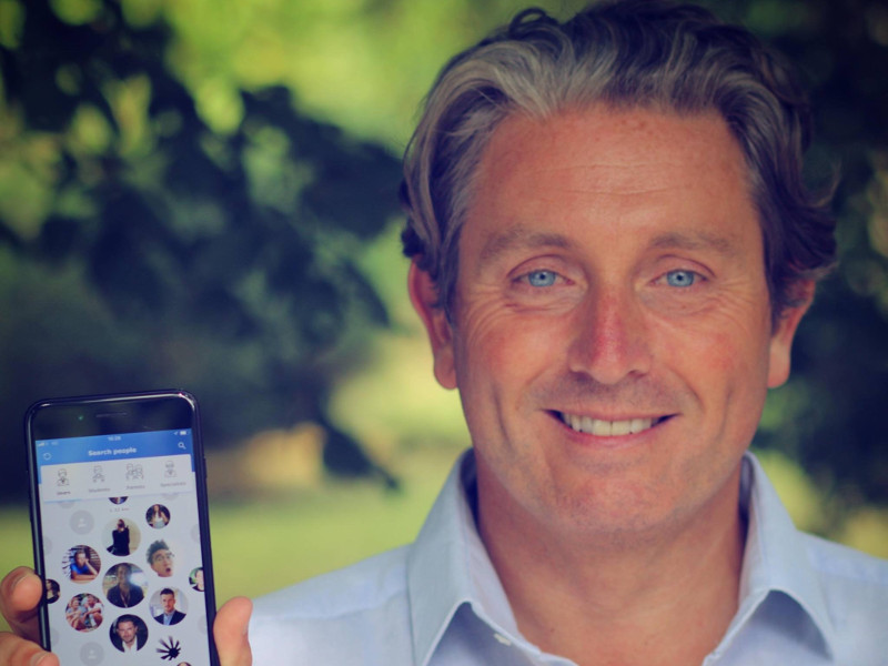 Smiling man with blue eyes holding a phone.