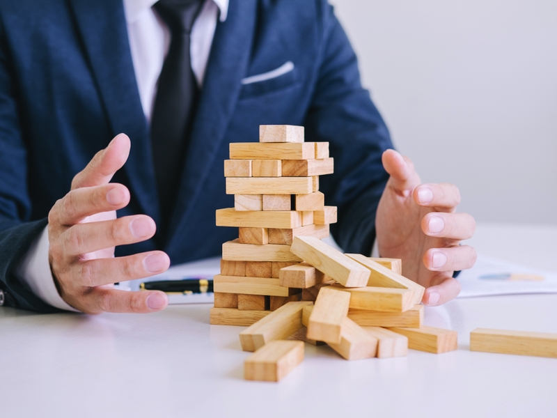 Business man in blue suit watches collapsed jenga tower.