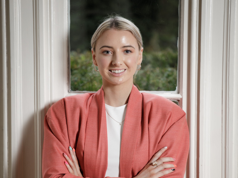 Young woman with blonde hair wearing pink jacket.