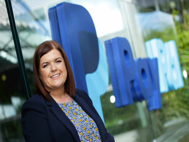 Dark-haired woman in front of a PayPal sign.