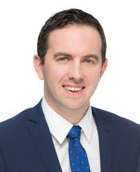 Dark haired man in suit with blue tie.