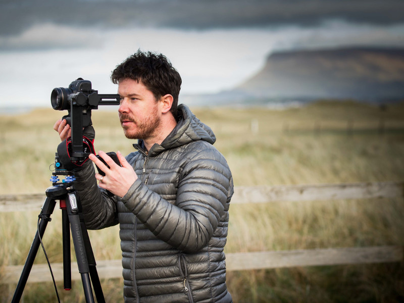 Man looking through camera in front of a mountain.