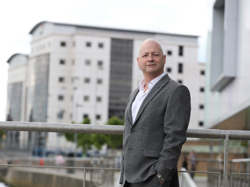 Man standing beside railing between buildings.