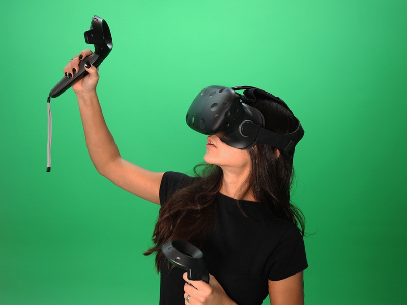 Woman using VR equipment against a green background.