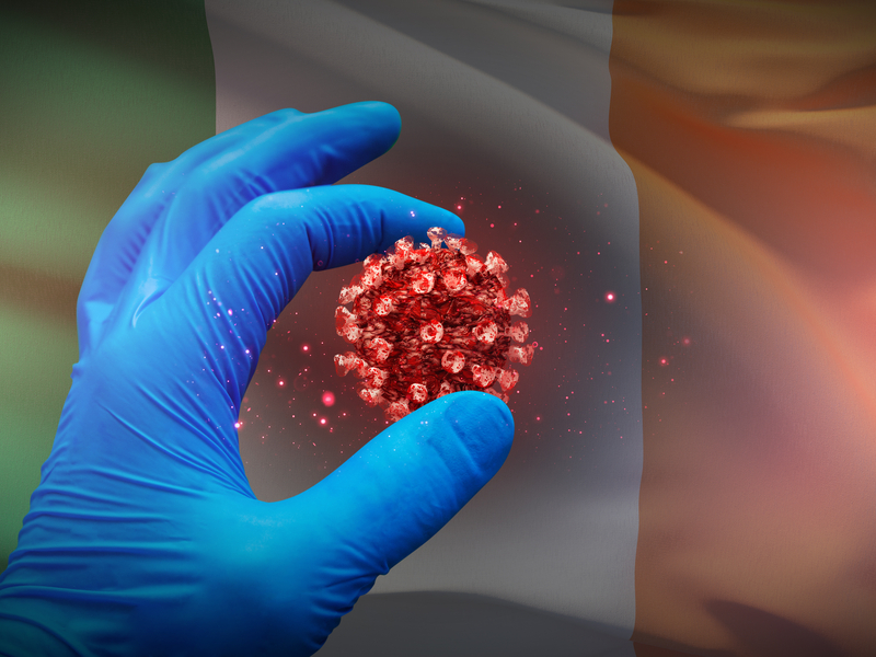 Gloved hand touching virus in front of Irish flag.