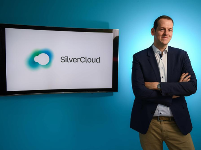 Man in navy jacket standing beside a screen with words SilverCloud on it.