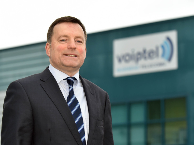 Man in suit standing beside a sign on a building saying Voiptel.