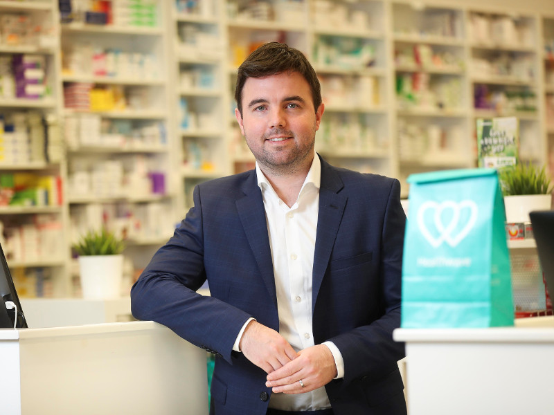 Man in navy jacket leaning on a counter in a pharmacy.