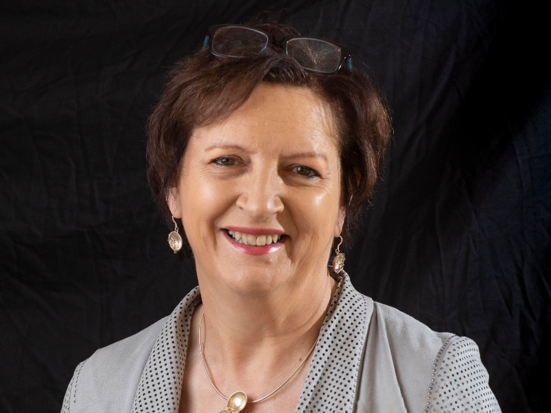 Dark-haired woman in grey jacket, smiling.