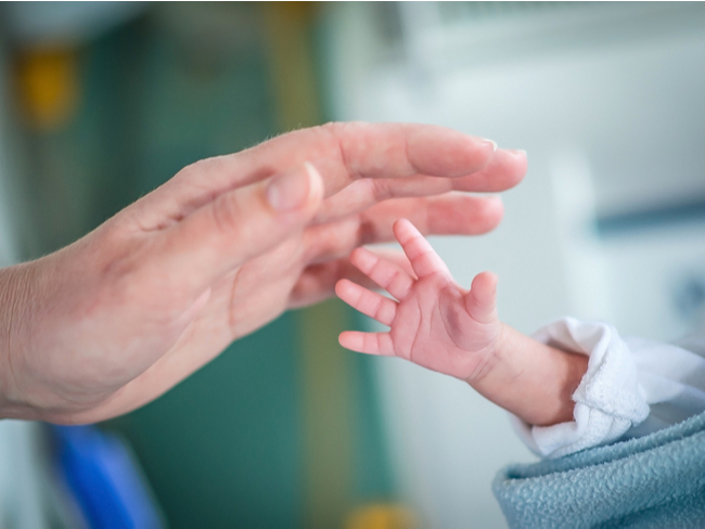 baby's hand reaches to an adult's hand.