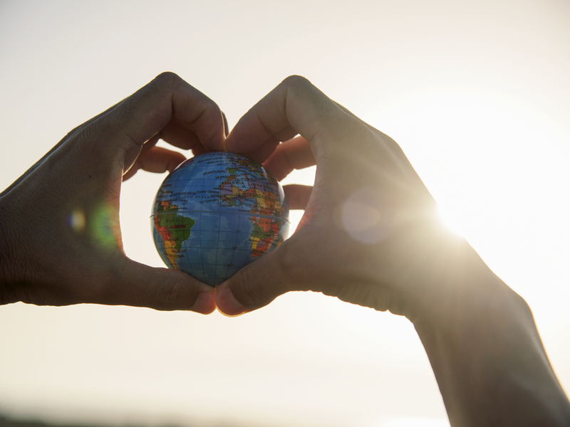 Hand making a love heart gesture while holding a globe.