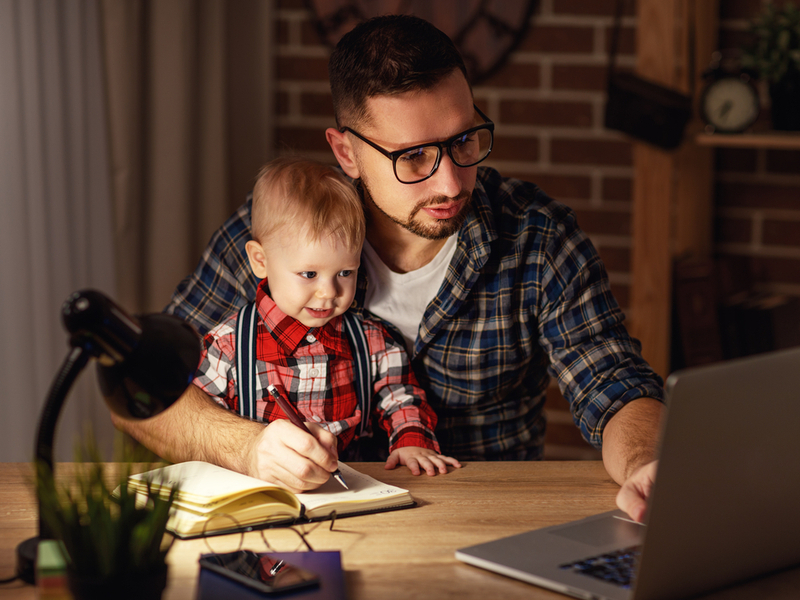 Father working from home holding son on knee.