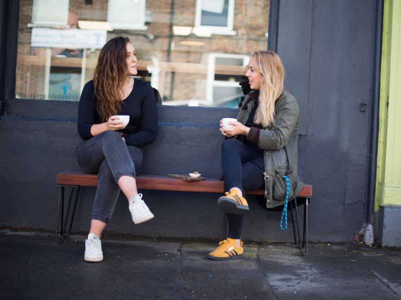 Two young women having coffee outside a shop.