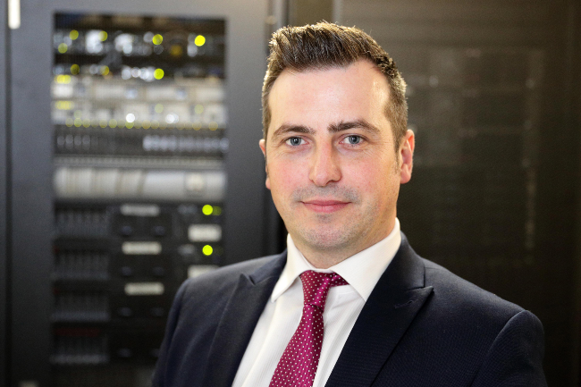 Dark haired man in suit and tie standing in a server room.