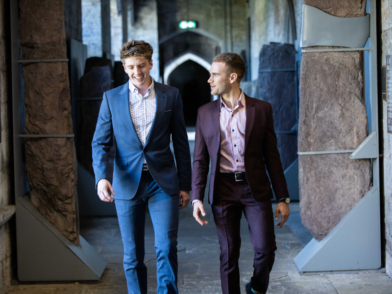 Two young men in suits walking a corridor.