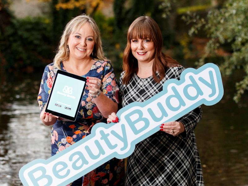 Two women holding a beauty buddy sign.