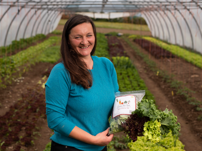 Woman in blue jumper in vegetable garden holding produce.