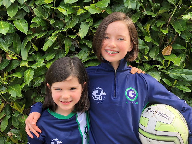 Two kids wearing navy jerseys holding a ball.