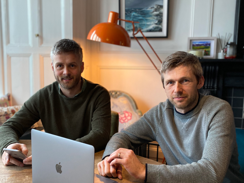 Two men sitting at a desk under glow of an orange lamp.