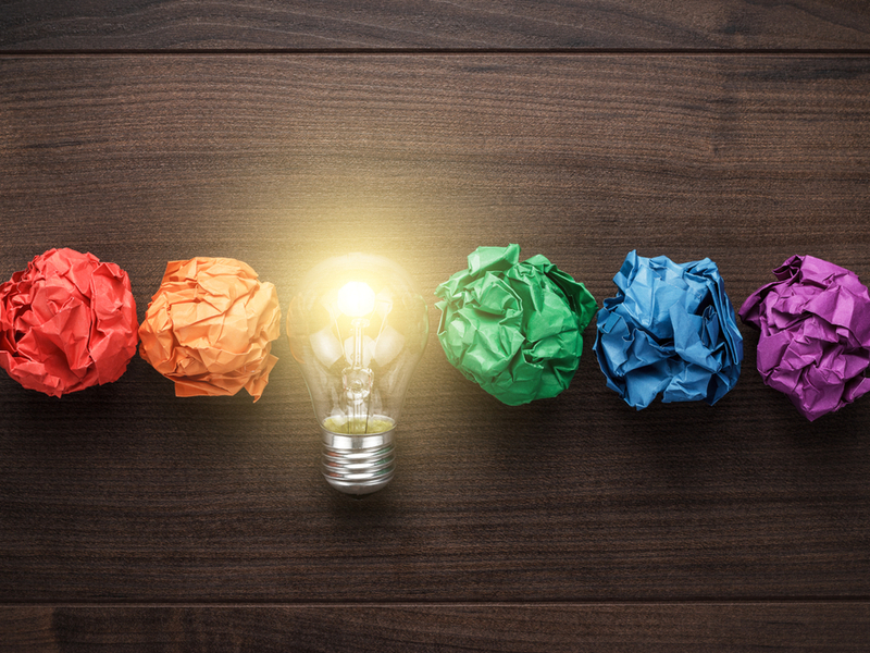 Crumpled bits of coloured paper alongside a switched on light bulb.