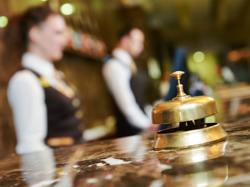 Lobby of a hotel with staff behind desk and bell in foreground.